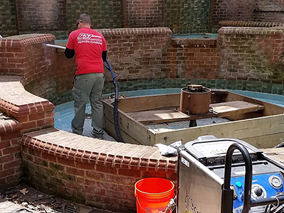 Worker pressure washing a drained fountain