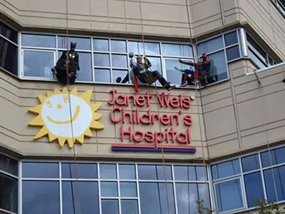 Workers dressed as super heroes clean glass windows on a children's hospital