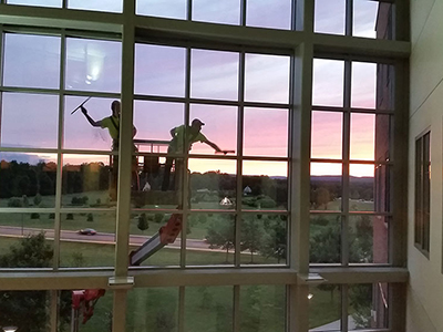 Workers clean glass windows on a low rise building while the sun sets in the background